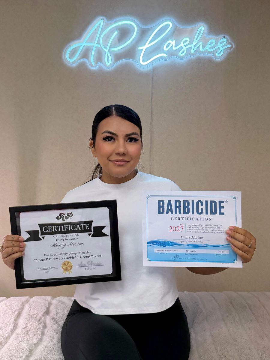 Graduate holding her certificate and Barbicide certification under the AP Lashes neon sign