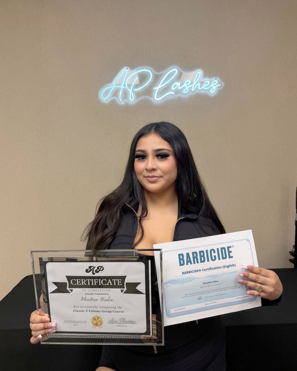 Graduate holding her framed certificate under the AP Lashes neon sign